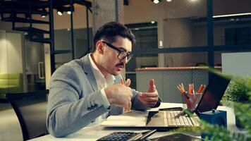 Professional man in office attire engaged in a focused discussion while using a laptop and taking notes at his desk during working hours video