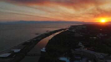 deslumbrante pôr do sol zangão voar sobre uma rio fluindo para dentro a mar atrás montanhas video
