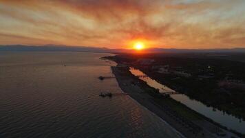 zangão tiro do rio fluindo para dentro a mar às pôr do sol atrás montanhas video