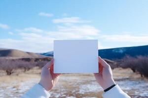 Hands holding a blank white piece of paper in front of a blue sky with white clouds. The image is simple and clean, with plenty of space for text. photo