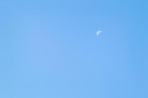 A beautiful crescent moon in the afternoon sky. A crescent moon in daylight against a clear blue sky. photo