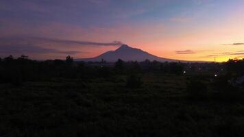 4k aerial footage of Mount Merapi at a distance of about 12 miles. Morning panorama of an active volcano from a distance after sunrise with rice fields and residential areas in the foreground video