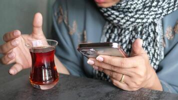 A person delightfully enjoying a warm cup of tea while simultaneously using their smartphone video