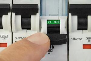 Hand turning off electrical circuit breaker in control panel photo