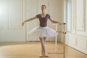 Young ballerina in tutu skirt stretching practicing ballet positions dancing near ballet barre in dance class. Young classical dancer woman in dance studio. Ballet class training Ballet school concept photo