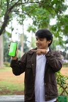Southeast Asian man showing something on his smartphone with a green screen, perfect for customizable content photo
