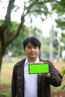 Southeast Asian man showing something on his smartphone with a green screen, perfect for customizable content photo