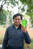 Southeast Asian man showing something on his smartphone with a green screen, perfect for customizable content photo
