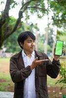 Southeast Asian man showing something on his smartphone with a green screen, perfect for customizable content photo