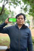 Southeast Asian man showing something on his smartphone with a green screen, perfect for customizable content photo