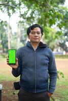 Southeast Asian man showing something on his smartphone with a green screen, perfect for customizable content photo
