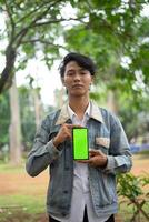 Southeast Asian man showing something on his smartphone with a green screen, perfect for customizable content photo