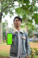 Southeast Asian man showing something on his smartphone with a green screen, perfect for customizable content photo