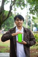 Southeast Asian man showing something on his smartphone with a green screen, perfect for customizable content photo