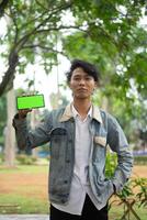 Southeast Asian man holding a smartphone with a green screen, pointing to something on the display. photo