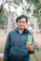 Southeast Asian man showing something on his smartphone with a green screen, perfect for customizable content photo