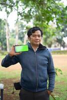 Southeast Asian man showing something on his smartphone with a green screen, perfect for customizable content photo