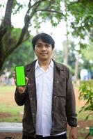 Southeast Asian man showing something on his smartphone with a green screen, perfect for customizable content photo