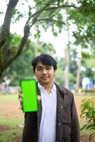 Southeast Asian man showing something on his smartphone with a green screen, perfect for customizable content photo