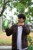 Southeast Asian man showing something on his smartphone with a green screen, perfect for customizable content photo