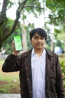 Southeast Asian man showing something on his smartphone with a green screen, perfect for customizable content photo