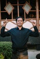 Southeast Asian man pointing upwards with both hands, conveying enthusiasm or inspiration. photo