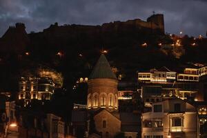A serene evening in Tbilisi, an illuminated old church against a dramatic skyline photo