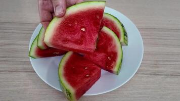 Hand picking juicy watermelon slices from a white plate, perfect for summer picnics and refreshing desserts video