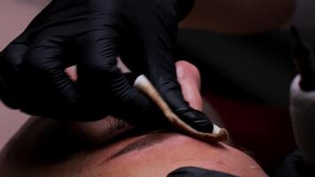 A close-up of the master wiping residual pigment from the eyebrows. Eyebrow tattoo procedure. video