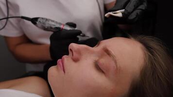 In front of the model sits the master who performs the procedure of tattooing and wipes excess pigment from the eyebrows. Light permanent eyebrow makeup, performing eyebrow tattooing video