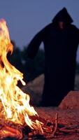Monk pray at the campfire. Man in a cassock performs around fire Vertical video