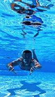 Vacation concept. Happy young man swimming inside the swimming pool. Man is diving under the water and moving forward to camera. Vertical video