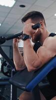 Bearded man pumping his arm muscles in the gym. Athletic bodybuilder training his biceps on a modern simulator and looking confidently forward. Vertical video