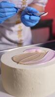 Pastry cook applies white cream with a spoon on top of the white cake. Close up. Chocolate cake at the table at backdrop. Vertical video