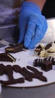 Hands in blue latex gloves cut the chocolate sweets on the plate. Preparation of desserts for demonstration and degustation. Close up. Vertical video