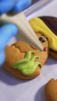 Gloved hands squeeze the creamy decoration from pastry bag on the cookies of mushroom shape. Biscuits icing on the tray. Close up. Vertical video