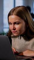 Resilient smiling woman working on computer pulls closer to the screen. Lady rejoicing looking at her laptop rising hands cheerfully. Vertical video