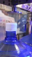Corking the bottles of fresh clean water. Big flasks filled with water move by the conveyor belt. Mineral water production at factory. Vertical video