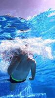 Underwater of a boy swimming in blue clear water. Little boy dives under the water with closed eyes in the swimming pool. Vertical video