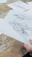Hands of a tailor putting papers with stylish sketches on the table. Modern creative works of a fashionable designer is sorting by a seamstress in atelier. Vertical video