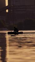 Fisherman in a boat with fishing rods in the evening. Man in hat floating in a boat and fishing on the background of a factory in the city. Vertical video