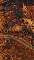 Two cars riding by the highway going through the desert landscape. Rounded rocks in the light of bright sun from aerial view. Vertical video