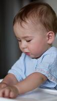 Lovely baby boy sitting at the feeding table playing cheerfully with food. Active toddler moving bagels by the table. Blurred backdrop. Vertical video
