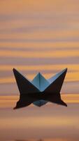 Origami boat on water surface in the evening. White paper boat swims with its shadow reflection in water. Close-up. Vertical video