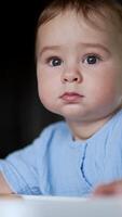 Serious thoughtful baby boy sitting at the table. Kid playing with food, throwing bagel on the floor and looking at it. Close up. Vertical video