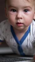 Adorable Caucasian baby boy lying on the floor crawls up to the camera. Close up. Blurred background. Vertical video