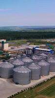 Enormous plant for storing and processing grain. Modern complex of grain elevators for keeping and drying crop. Drone view. Beautiful nature scenery at the background. Vertical video