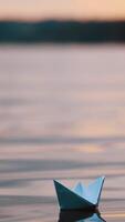 Blue homemade boat on water on blurred evening background. Paper little ship floating alone in calm river at sunset. Vertical video