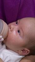 Sleepy baby finishing his milk in the bottle. Little child in mother's arms falling asleep gradually while having meal. Close up. Vertical video
