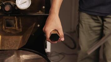 A hand is opening the discharge port on a coffee roasting machine with a lever pointing upwards. video